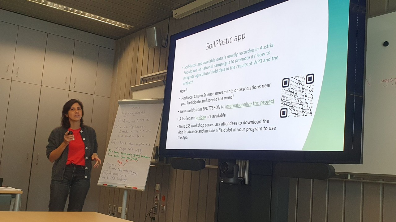 Researcher in front of presentation, on the presentation are information on the SoilPlastic App